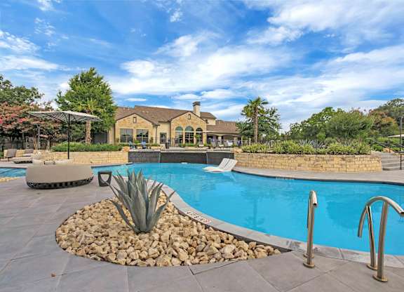 Curved pool edge with stone landscaping, agave plantings, and handrails at entry.