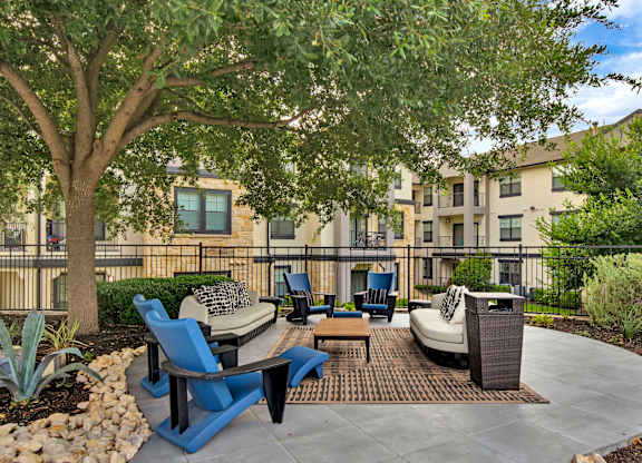 Outdoor lounge area with cushioned seating under a shade tree and patterned rug.