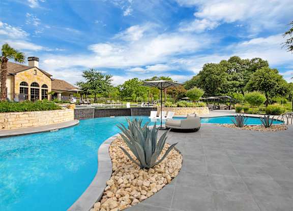 Poolside view with in-water loungers, umbrella seating, and lush green landscaping.