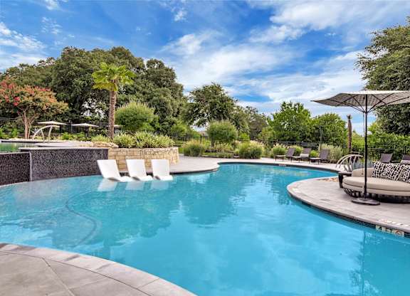 Swimming pool with in-water chaise loungers, shaded daybed, and lounge chairs.