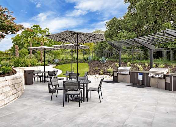 Community grilling pavilion with covered stations, patio tables, and umbrella seating.