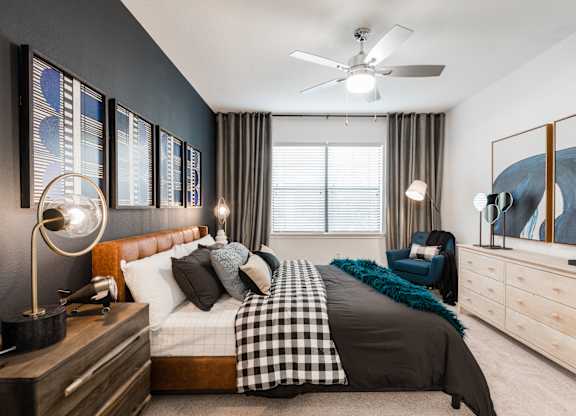 Primary bedroom with ceiling fan, upholstered bed, accent wall, and large window.
