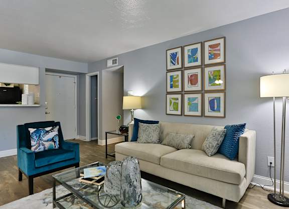 A living room with a blue chair, a beige couch, and a glass coffee table.