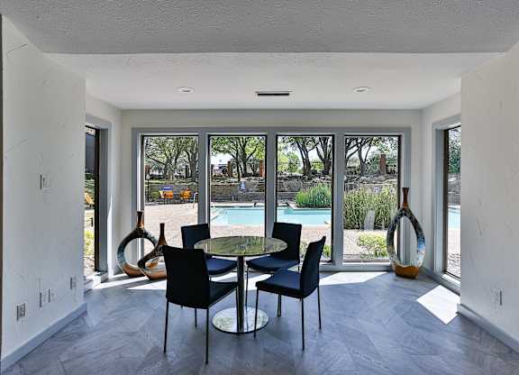 A dining room with a table and chairs and a view of a pool and trees outside.