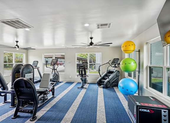 a gym with treadmills and other exercise equipment in a room with windows