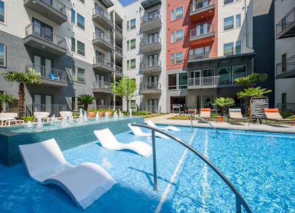A swimming pool with white lounge chairs in front of apartment buildings.