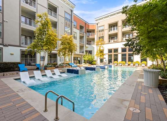 A pool surrounded by chairs and trees in front of apartment buildings.