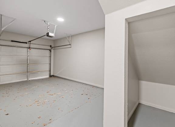 Attached garage interior with overhead door, painted concrete floor, and under-stair storage nook.