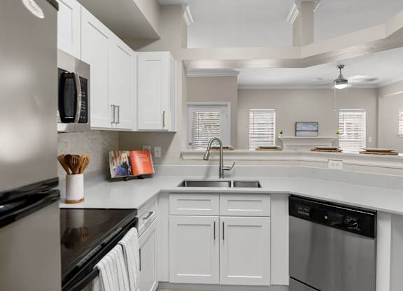 Open kitchen with breakfast bar, double-basin sink, dishwasher, and view into living area.