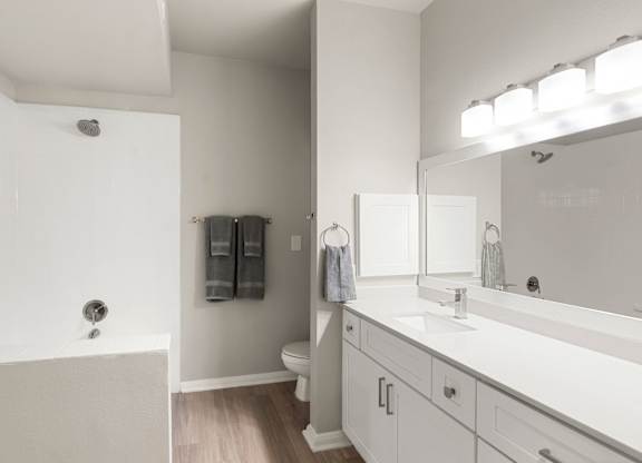 Bathroom with long single-sink vanity, soaking tub, white tile surround, and modern lighting.