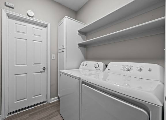 Laundry room with full-size washer and dryer, upper shelving, and storage cabinet.