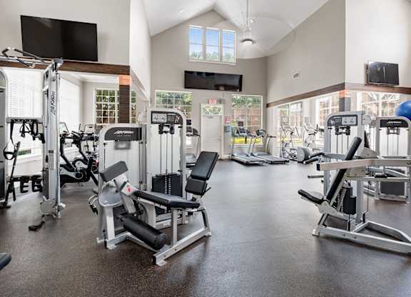 Spacious fitness center with strength machines, cardio equipment, vaulted ceilings, and large windows.