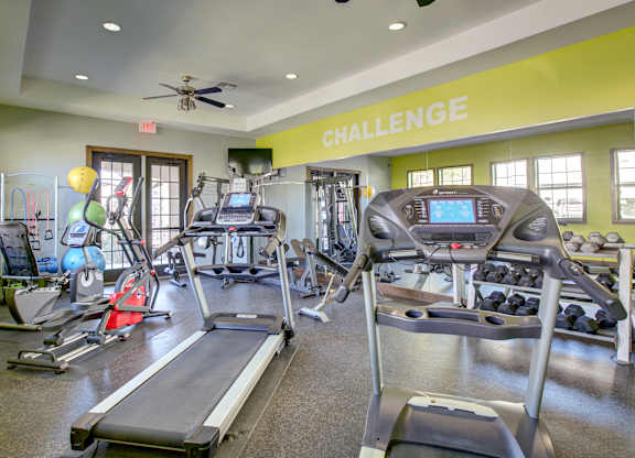 Expansive fitness room with cardio equipment, weight racks, and mirrored wall.