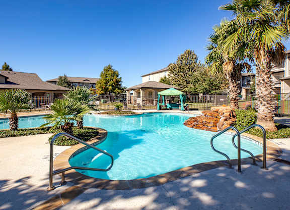 Sparkling pool with shaded cabana, palm landscaping, and rock water feature.
