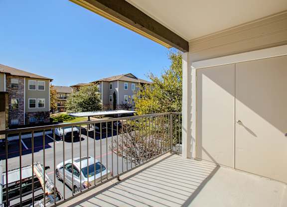 Private balcony with railing and outdoor storage, overlooking community parking area.