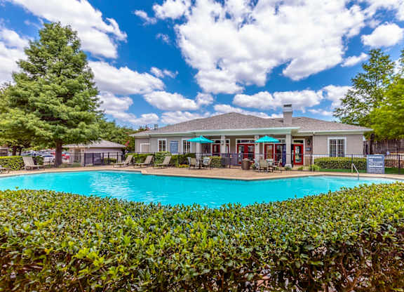 A pool surrounded by green bushes with a house in the background.