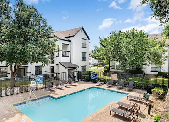 Smaller community pool with lounge chairs, fenced deck, and surrounding apartment buildings.