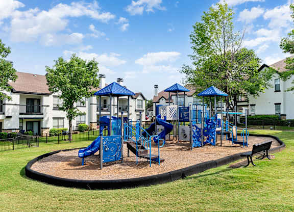 Community playground with blue climbing structures and slides set on a grassy lawn.