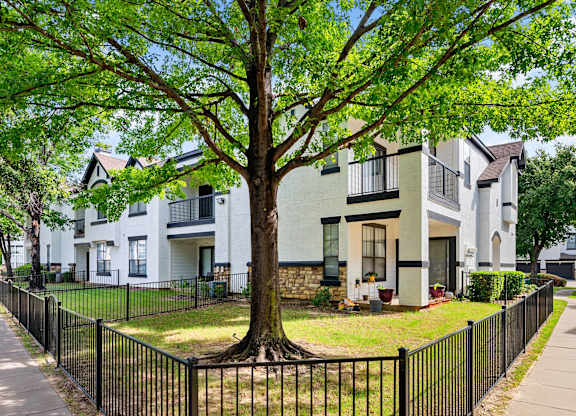 Apartment exterior with fenced yard, private patio, balconies, and mature shade tree.