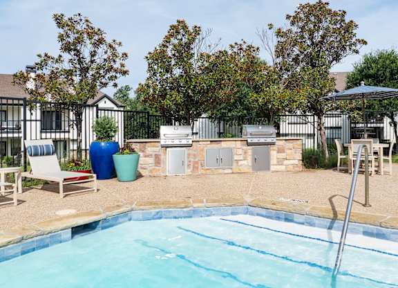 Poolside grilling area with two barbecue stations, lounge seating, and shaded outdoor table.