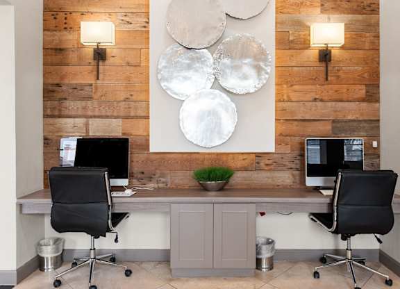 Business center with two desktop computers, leather chairs, and wood accent wall.