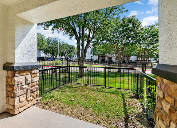 Covered patio with stone columns and fenced grassy yard at Villas of Vista Ridge.