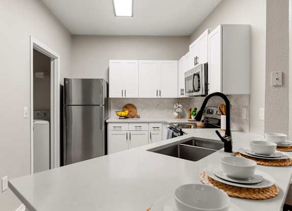 Modern kitchen with white cabinetry, breakfast bar, laundry closet, and stainless steel appliances.