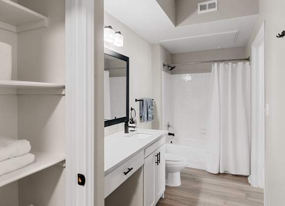 Bathroom with single vanity, large framed mirror, open shelving, and tub-shower combination.