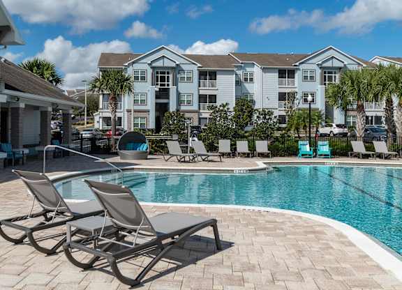 a swimming pool with chaise lounge chairs and a resort style building in the background