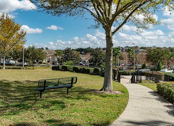 a park bench in a grassy area with trees and houses in the background