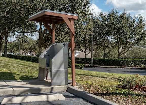a parking meter in a park with trees in the background