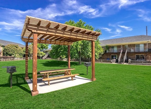 A wooden pergola with a bench is situated in a grassy area.