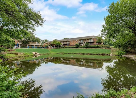 A serene landscape with a pond, trees, and a building in the background.