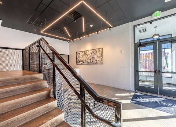 A staircase with a metal railing leads to a brightly lit room with a large painting on the wall.