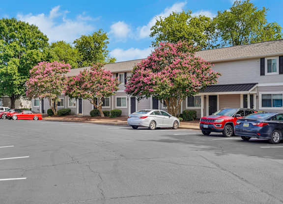A parking lot with cars and a building with trees in front.
