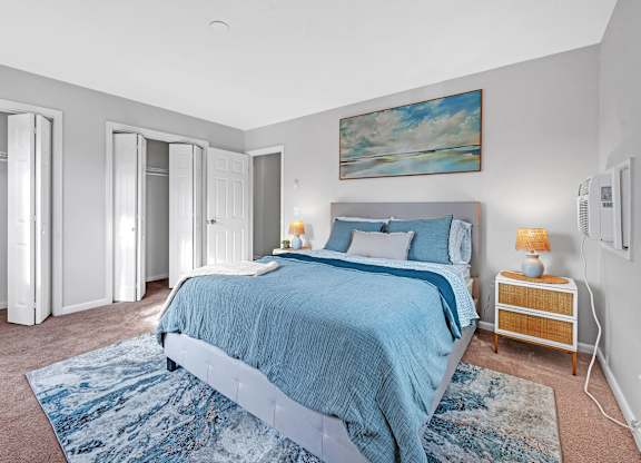 A bedroom with a blue bedspread and a painting on the wall.