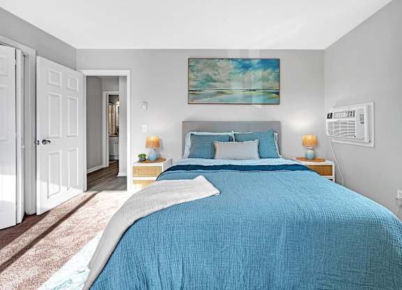 A bedroom with a blue bedspread and a painting on the wall.