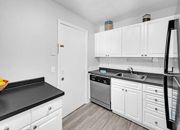 A kitchen with white cabinets and black countertops.