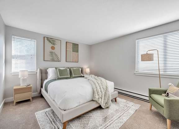 A bedroom with a large bed, a green chair, and two lamps.