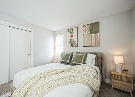 A bedroom with a bed covered in a white blanket and pillows.