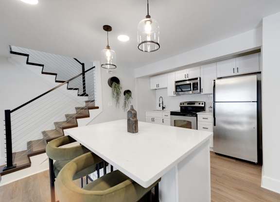 A modern kitchen with a white island and a staircase.
