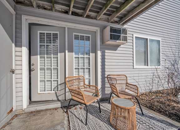 Two chairs and a table are on a porch.