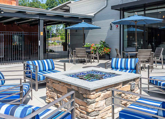 A patio with blue and white striped chairs and a stone fire pit.
