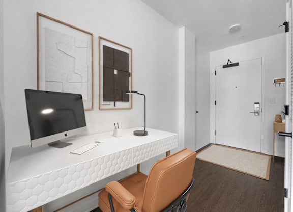 A white desk with a computer monitor, keyboard, and mouse is in a room with a brown chair and two framed pieces of artwork on the wall.