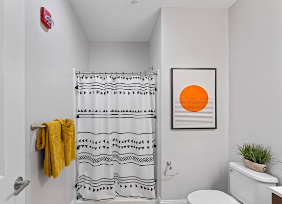 A bathroom with a yellow towel hanging on the door and a shower curtain with black and white designs.