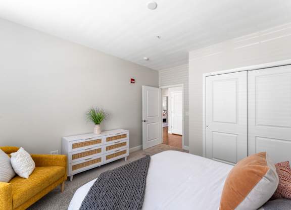 A bedroom with a bed, a yellow sofa, and a wooden dresser.