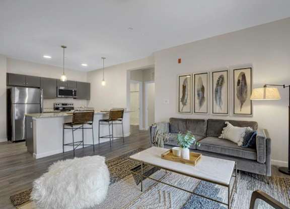 A modern living room with a grey couch, a white coffee table, and a kitchen area in the background.