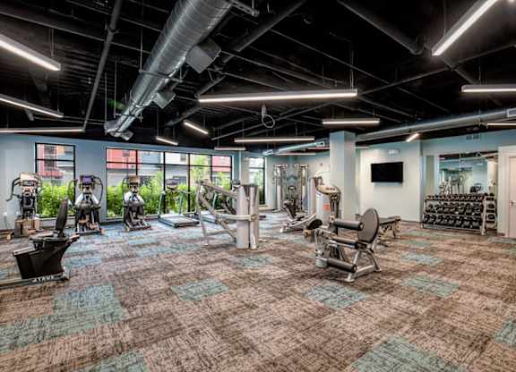 a gym with weights and cardio equipment in a large room with windows