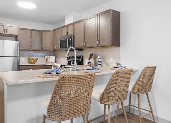 A kitchen with a white countertop and brown chairs.