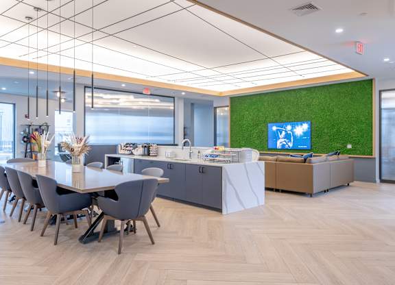 A conference room with a long table and chairs, a reception desk, and a green wall with a TV at Seacoast Residences Apartments, Oakland, ME